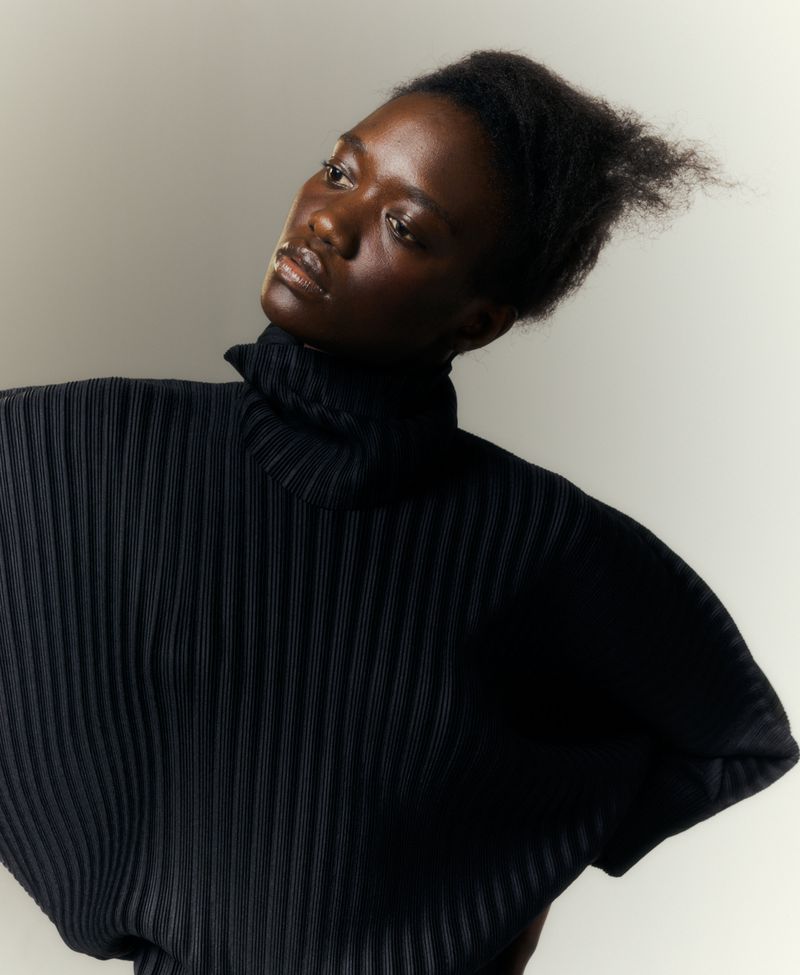 The Power Players: Mary N'Diaye by Antoine Harinthe for Matches Fashion Spring-Summer 2021 Ad Campaign. Clothing: Pleats Please Issey Miyake Black Roll-neck dolman-sleeve technical-pleated top / Pleats Please Issey Miyake Black Cropped technical-pleated trousers / CO Black Cross-strap leather sandals