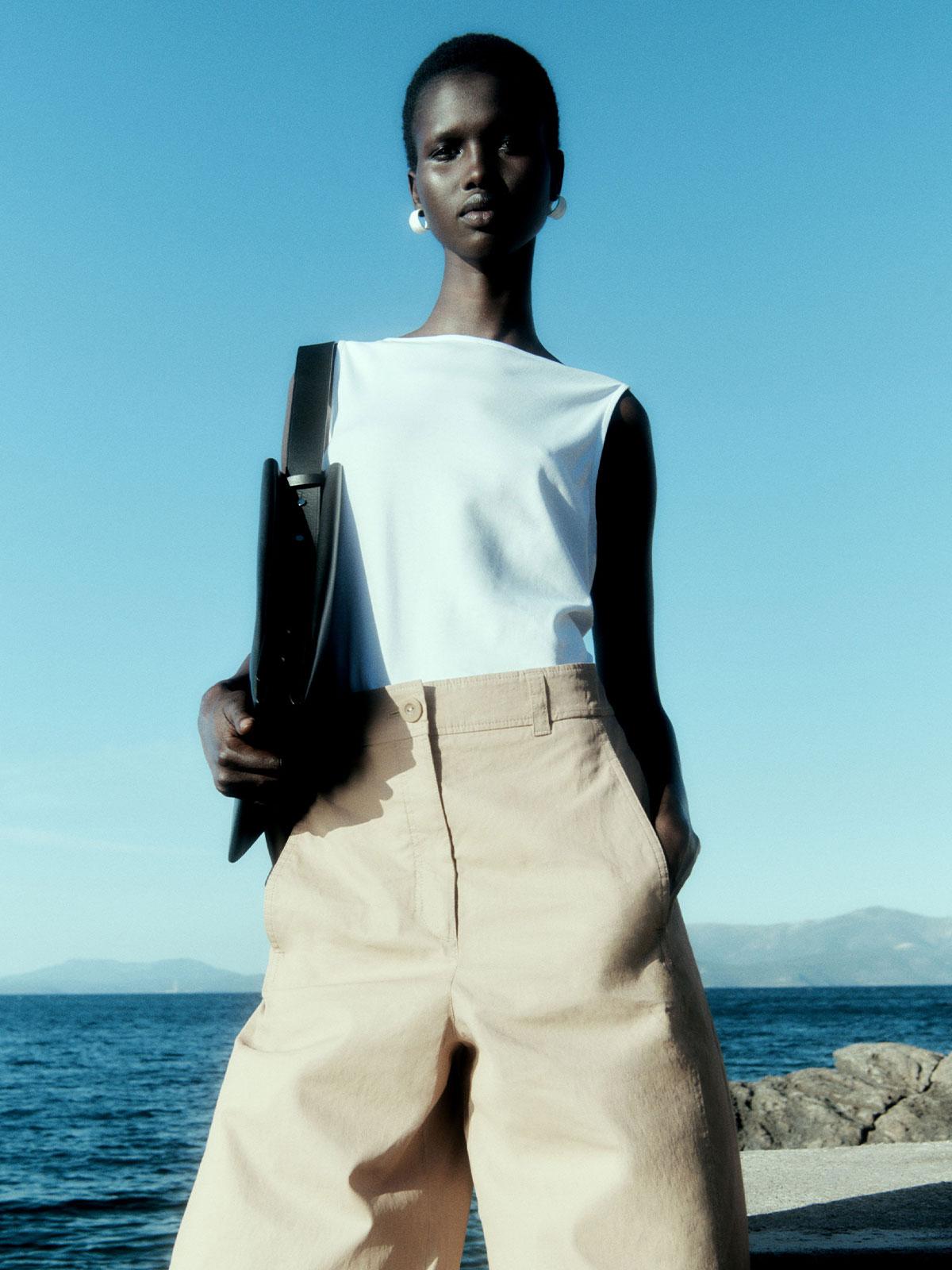 Amar Akway by Robin Galiegue for COS Summer 2021 Ad Campaign. Clothing: COS WHITE BOAT-NECK VEST / COS BEIGE WIDE-LEG LINEN PANTS / COS BLACK LEATHER MINI BAG / COS WHITE TEXTURED HOOP EARRINGS