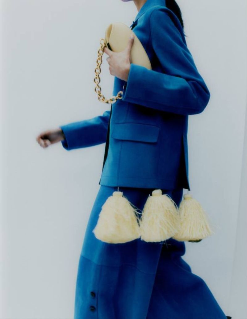 Chawntell Kulkarni by Umit Savaci for How to Spend It Magazine November 2021 Clothing & Accessories: Loewe pompom-embellished suede blazer and matching trousers. Salvatore Ferragamo nappa leather F-Heel shoes. Yuzefi leather Dinner Roll bag
