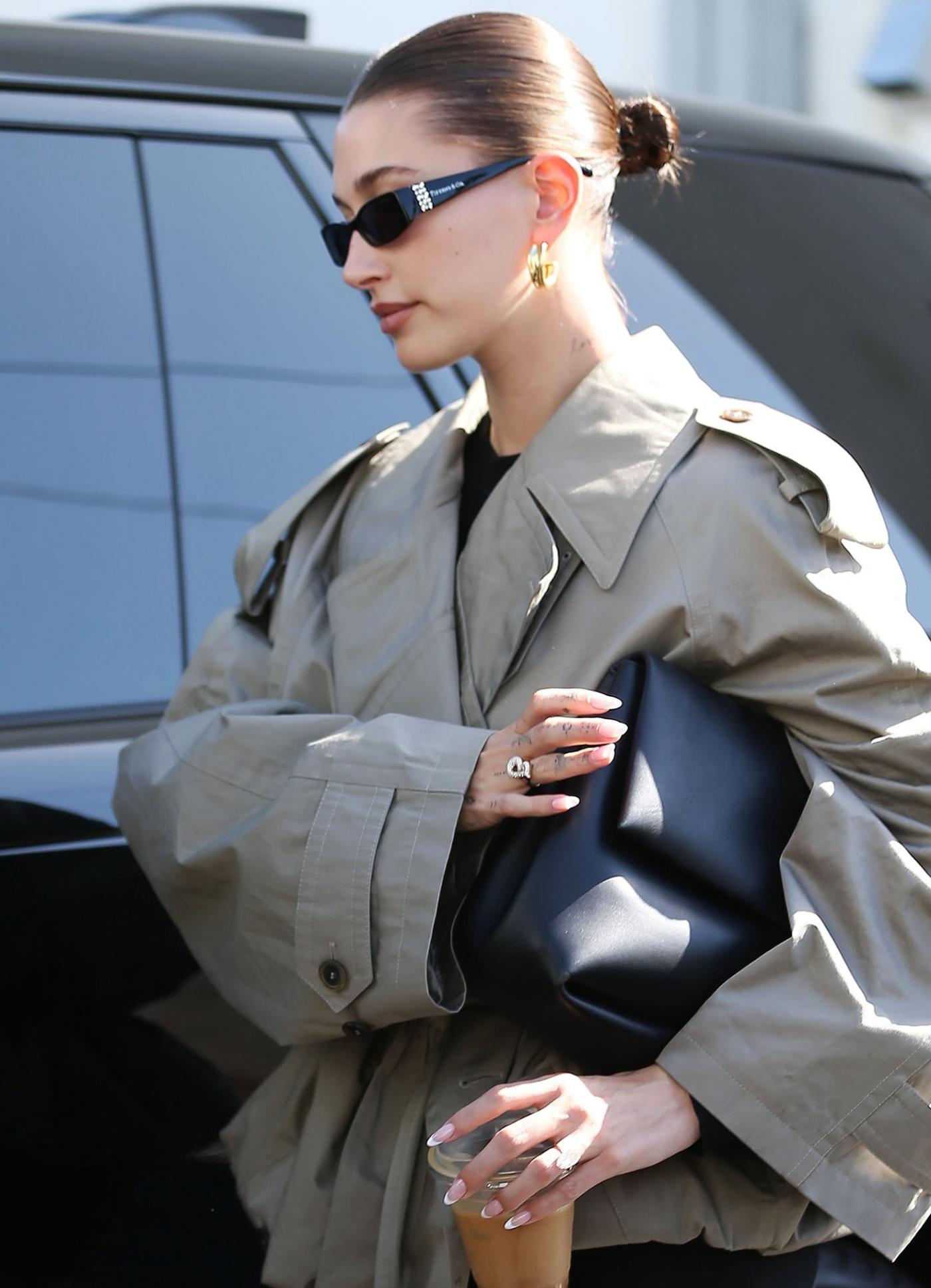 Hailey Bieber wears Balenciaga Beige Folded Trench Coat, Bottega Veneta Black Falcon Leather Clutch Bag, Tiffany & Co. Sunglasses Outfit