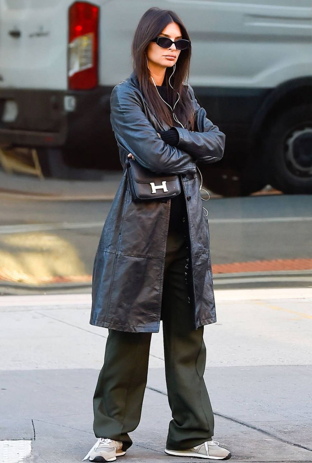 Emily Ratajkowski in New York City wearing Leather Trench Coat, Hermes Constance Bag, Green Pants, New Balance 574 Sneakers